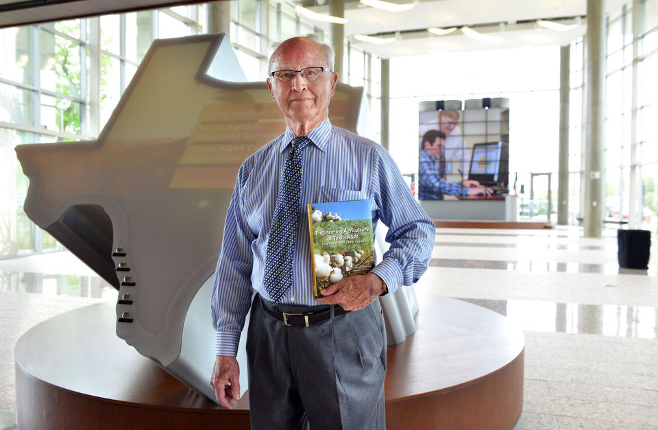 Sam Craft/The Eagle Author Henry Dethloff stands inside the Norman Borlaug Institute with his new book, Engineering Agriculture at Texas A&M: The First 100 Years, on Thursday. The book chronicles 100 years of history in the A&M agriculture department.