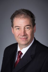 Dean Stover is posing for a classic portrait wearing a black suit with a maroon tie.