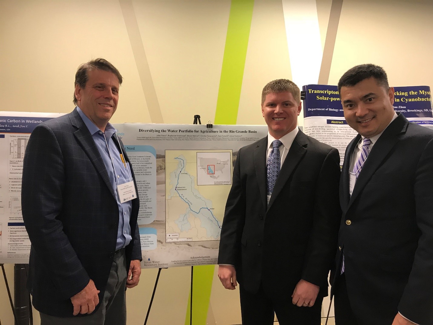 Three men in suits are standing by a map of a river system.