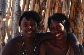 Two Damara women sit in the shade at their village during a hot afternoon.