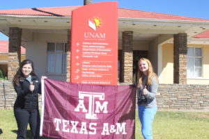 Alicia Torres and Natalie Grote hoisting a Texas A&M flag at the University of Namibia at Neudamm campus during an informal campus tour.