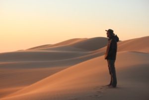 Living Desert Excursion tour guide, Chris, gazes over the sandy dune landscape of Dorob National Park, located north of the settlement of Swakopund in Namibia at dusk.