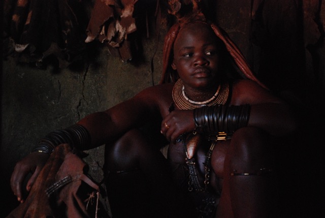 A Himba woman demonstrates how to bathe in smoke in the chief’s hut and applies red clay mixture. The women practice this routine daily in their own huts. 
