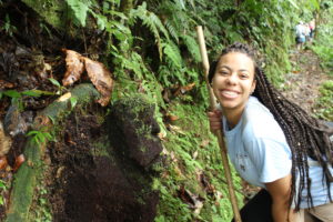 Felice Yarbough smiles alongside a friendly face shaped rock on the Soltis Center hiking pathway in the mountain.