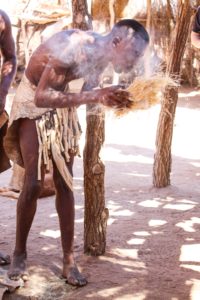 A Damara man at the Damara Living Museum demonstrates his ability to make fire using friction with a wooden stick, then blows on the smoke to catch the brush on fire. Skills such as making fire with minimal resources is essential to survival for communal landowners. 