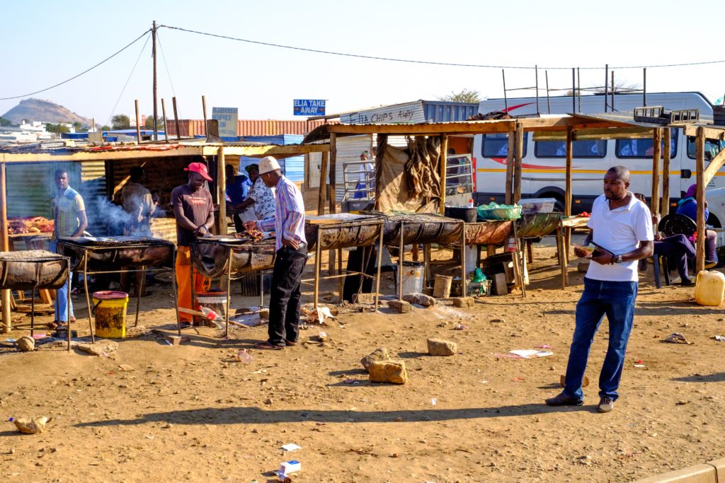 Katutura men are buying and selling lunch in a typical roadside market. There are many roadside businesses in Katatura including auto shops, markets, and barber shops.