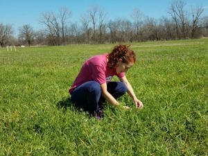 Diana Zapata kneeling in field looking at plants